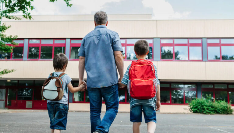 Padre llevando a sus dos hijos de la mano al colegio