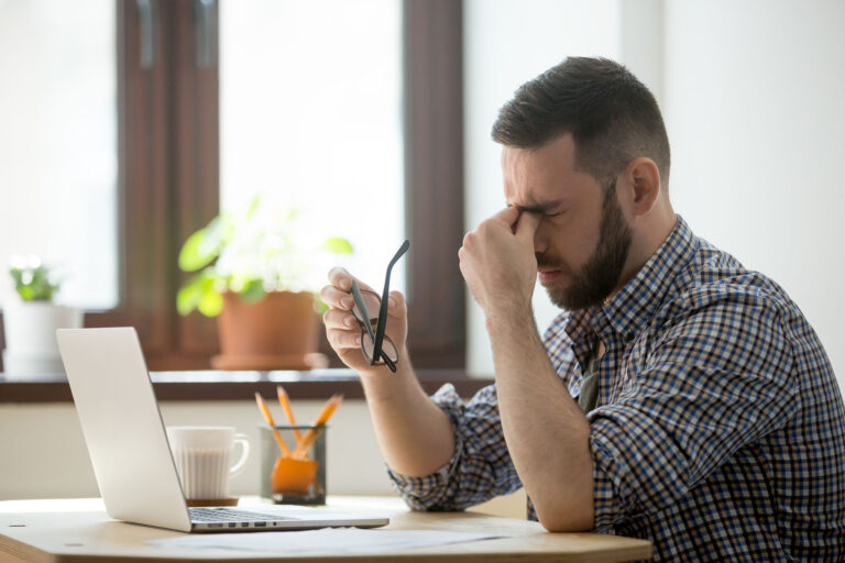 Hombre sentado en su oficina llevandose las manos a los ojos sufriendo de estrés y ansiedad