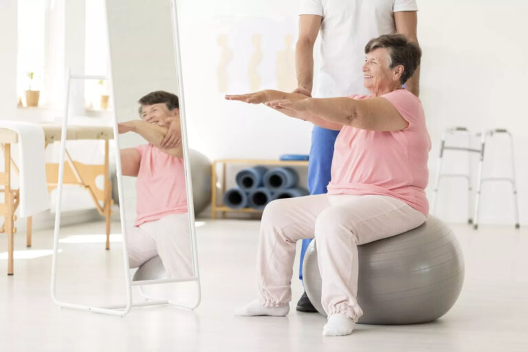 Mujer de edad avanzada practicando ejercicio sobre una bola de pilates en la Clínica Crisalud