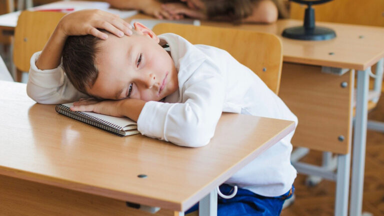 Niño en clase sentado y apoyando su cabeza sobre la mesa triste y deprimido